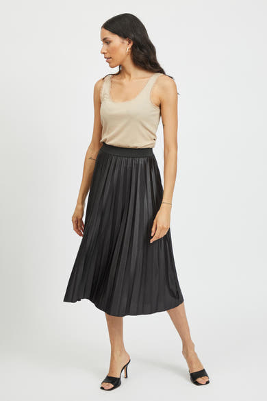 Zwarte geplooide midi-rok van VILA®, gedragen met een beige hemdje met kant en zwarte muiltjes.