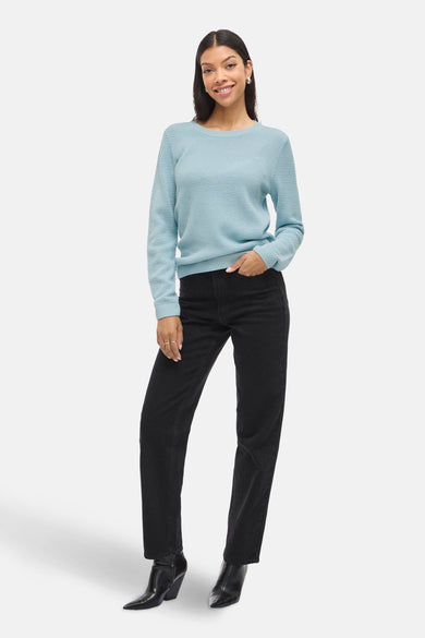 Pull bleu à col rond de VILA, porté avec un pantalon noir taille haute et des bottines en cuir.