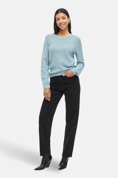 Pull bleu à col rond de VILA, porté avec un pantalon noir taille haute et des bottines en cuir.
