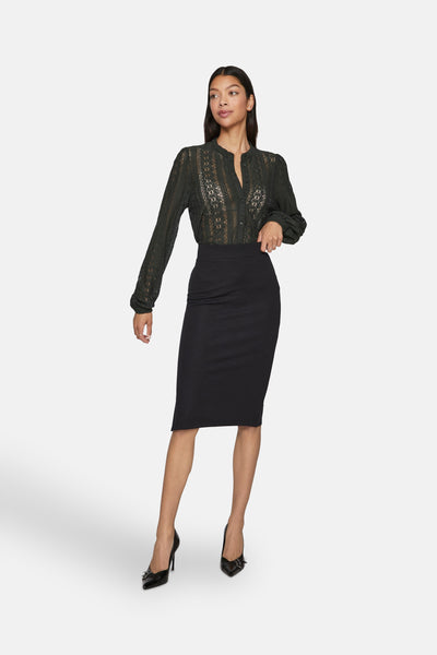 Chemise à manches longues verte de VILA, en dentelle florale semi-transparente, portée avec une jupe noire crayon et des escarpins noirs.
