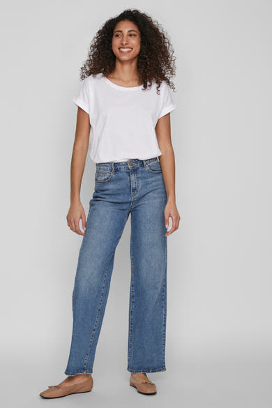 Top blanc uni à manches courtes de VILA, porté avec un jean bleu taille haute et des ballerines marron.
