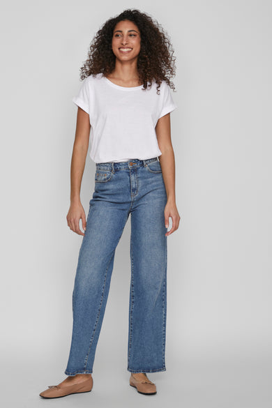 Top blanc uni à manches courtes de VILA, porté avec un jean bleu taille haute et des ballerines marron.
