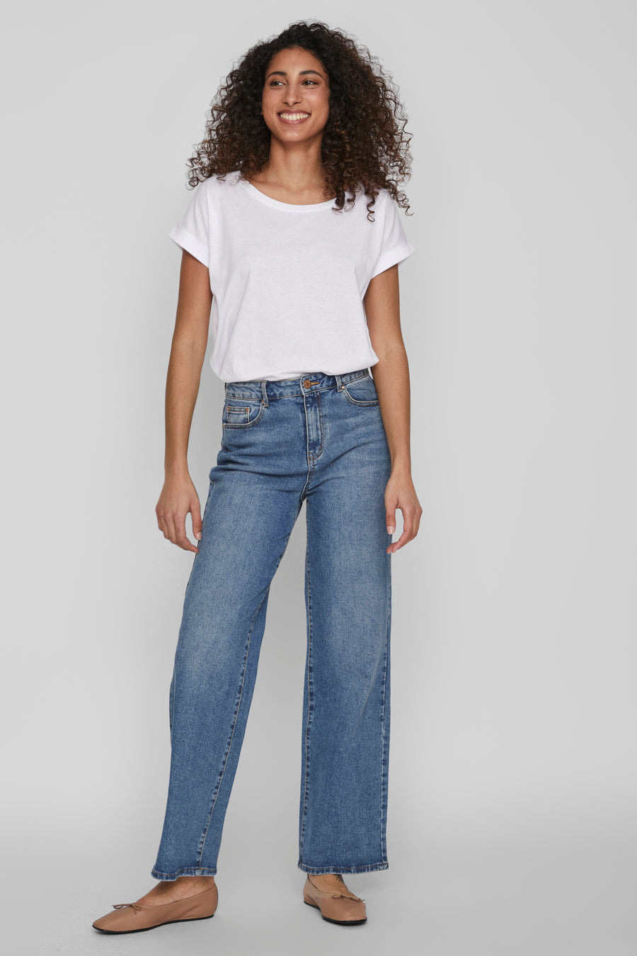 Top blanc uni à manches courtes de VILA, porté avec un jean bleu taille haute et des ballerines marron.

