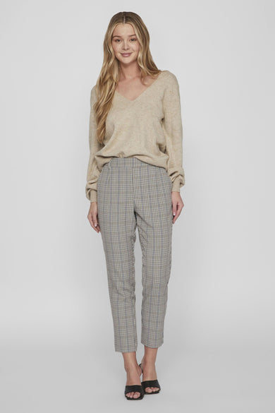 Pull col V beige de VILA, porté avec un pantalon à carreaux et des mules noires.