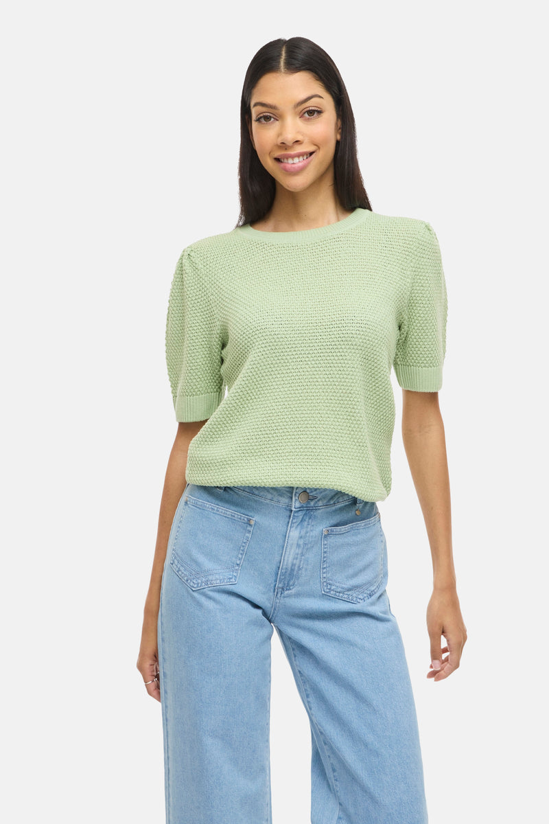 Pull vert en maille de VILA®, porté avec un jean taille haute bleu clair.
