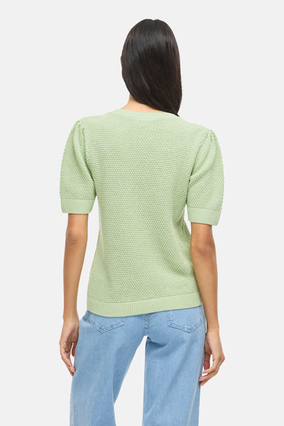 Pull vert de VILA, en tricot avec manches courtes bouffantes, porté avec un jean bleu clair.