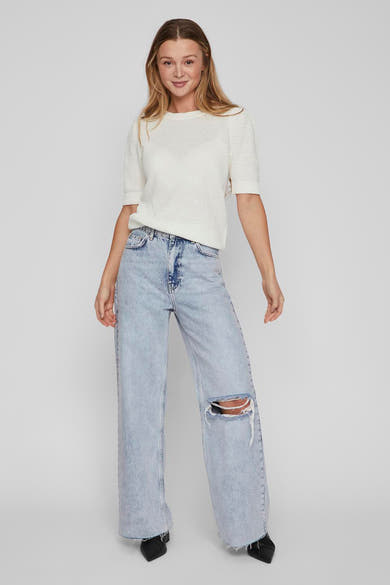 Pull blanc en maille de VILA®, porté avec un jean bleu ample et déchiré.