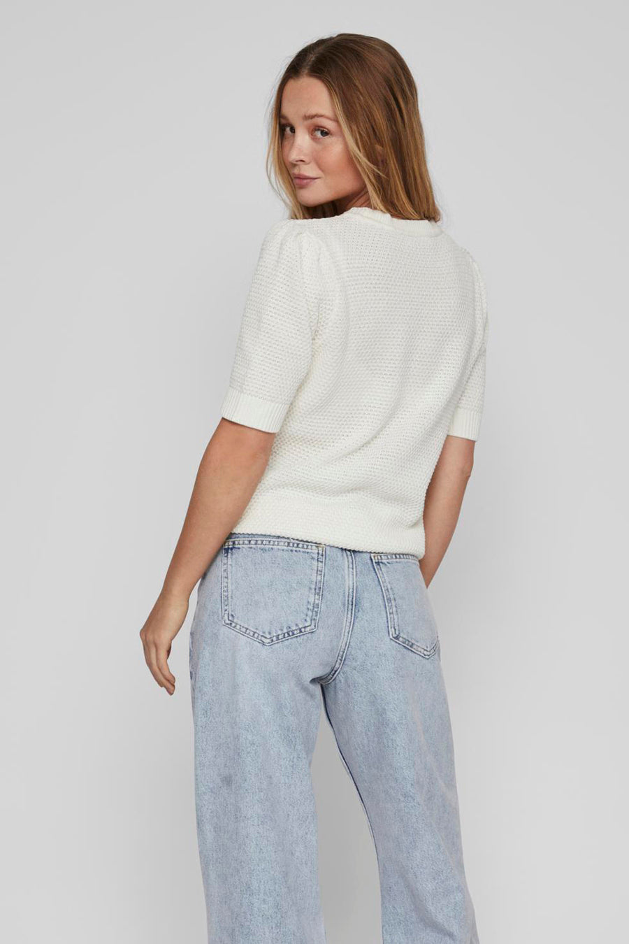 Pull blanc à manches courtes de VILA, en maille texturée, porté avec un jean taille haute.
