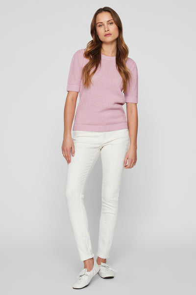 Pull rose en maille de VILA, porté avec un pantalon blanc et des baskets blanches.