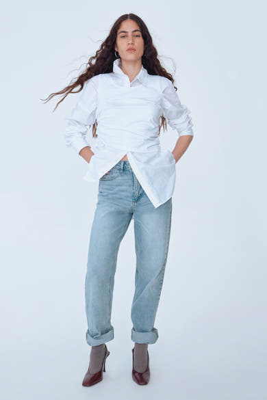 Wijde blauwe jeans van VILA®, gedragen met een wit overhemd en bruine hakken.