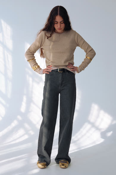 Grijze wijde jeans van VILA, gedragen met een beige trui, gouden armbanden en gouden schoenen.