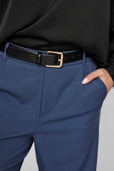 Blauwe broek van VILA, met zwarte leren riem en gouden gesp, hand in de zak.