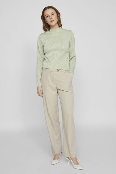 Top vert uni à manches longues de VILA, avec une texture plissée ondulée et porté avec un pantalon beige.
