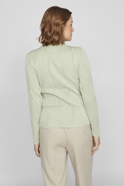 Top uni à manches longues vert de VILA, avec texture plissée ondulée, porté avec un pantalon beige.

