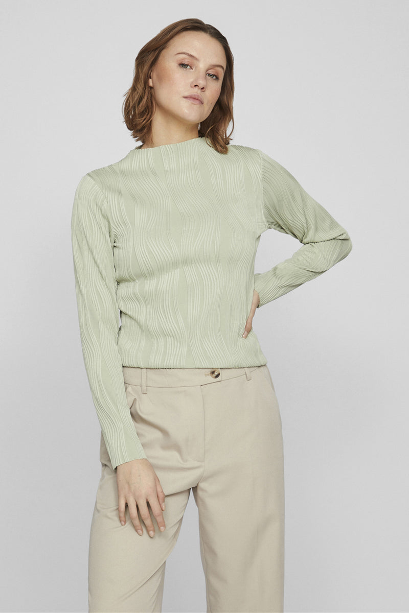 Top vert à manches longues par VILA®, avec motif texturé ondulé, porté avec un pantalon beige.
