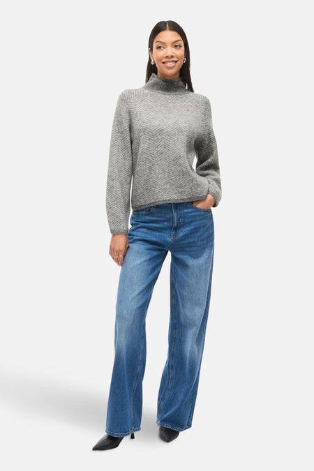 Pull à col roulé gris by VILA, avec motif chevrons et porté avec un jean ample bleu.
