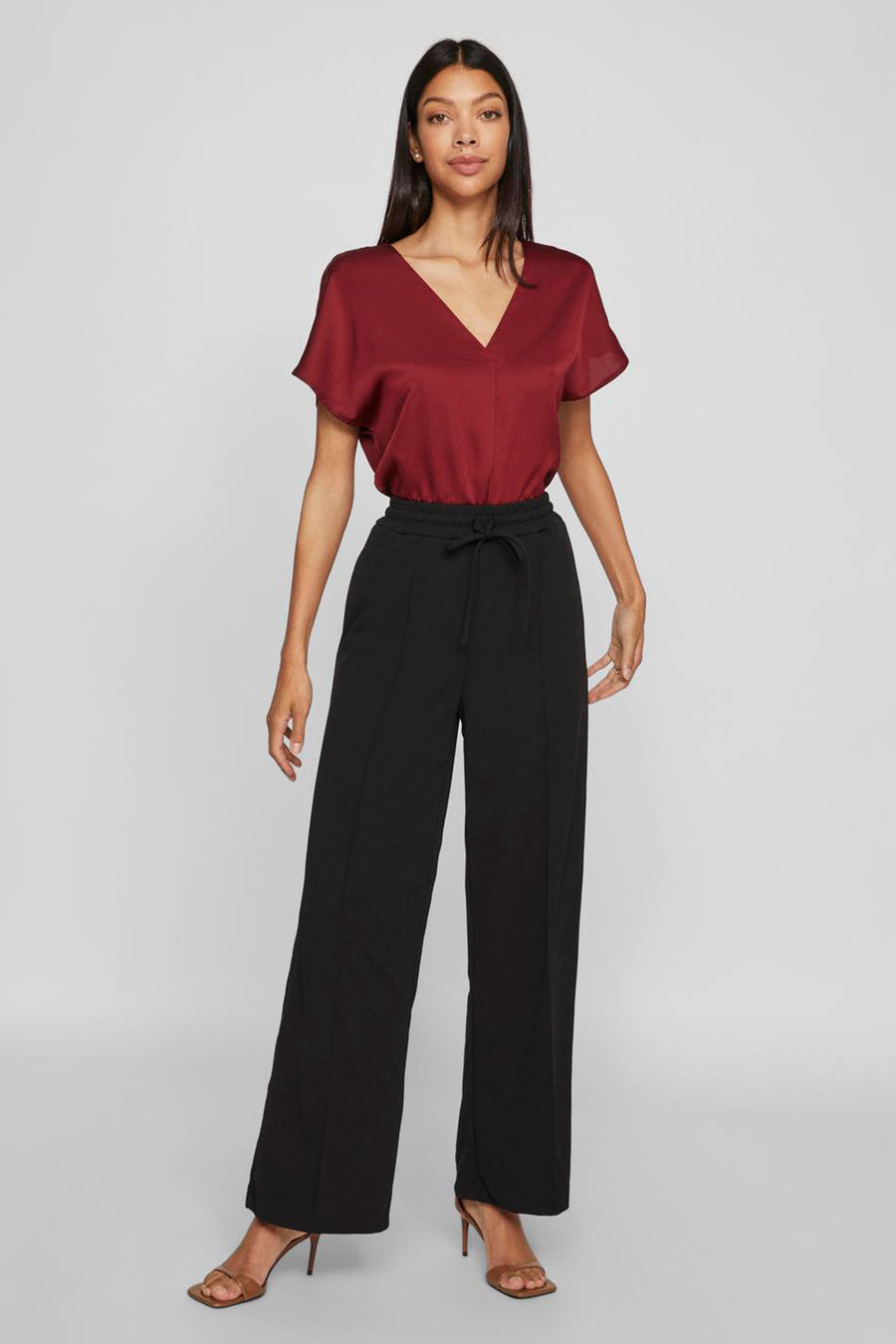 Zwarte broek VILA®, wijde pijpen en trekkoord in de taille, gedragen met een rode top en sandalen met hak.