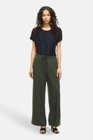 Groene broek van VILA, met trekkoord in de taille en wijde pijpen, gedragen met een zwart geplooid topje en zwarte hoge hakken.