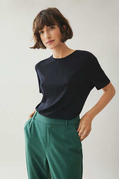 T-shirt noir à manches courtes de VILA®, porté avec un pantalon vert émeraude.
