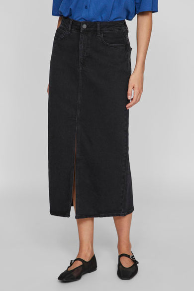 Jupe midi noire de VILA®, fendue sur le devant, portée avec un chemisier bleu et des ballerines noires.
