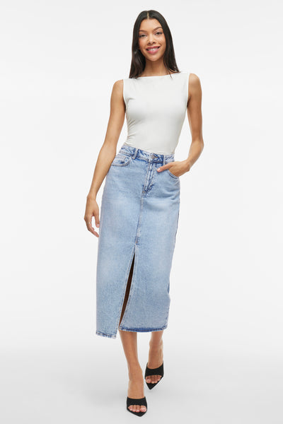 Jupe 3/4 en denim bleu clair de VILA, avec une fente à l'avant, portée avec un haut blanc uni.