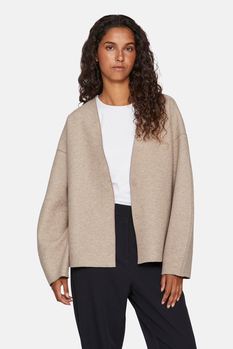 Korte beige jas van VILA, met wijde mouwen en een rechte zoom, gedragen met een zwarte broek.