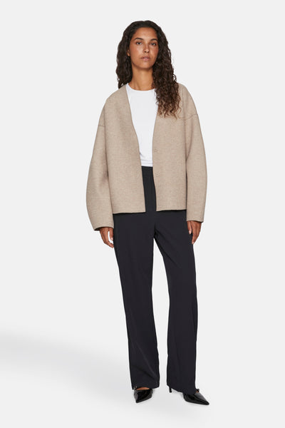 Veste courte beige de VILA®, portée sur un t-shirt blanc uni et un pantalon noir ample.

