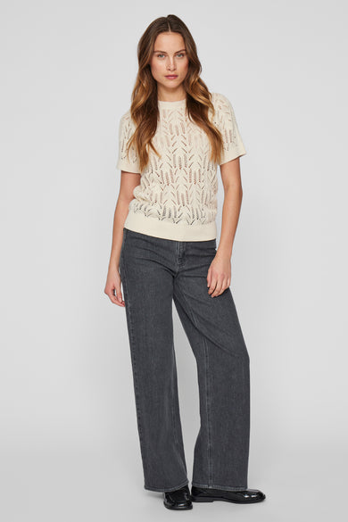 Pull écru à col rond par VILA®, porté avec un jean gris et des chaussures noires vernies.