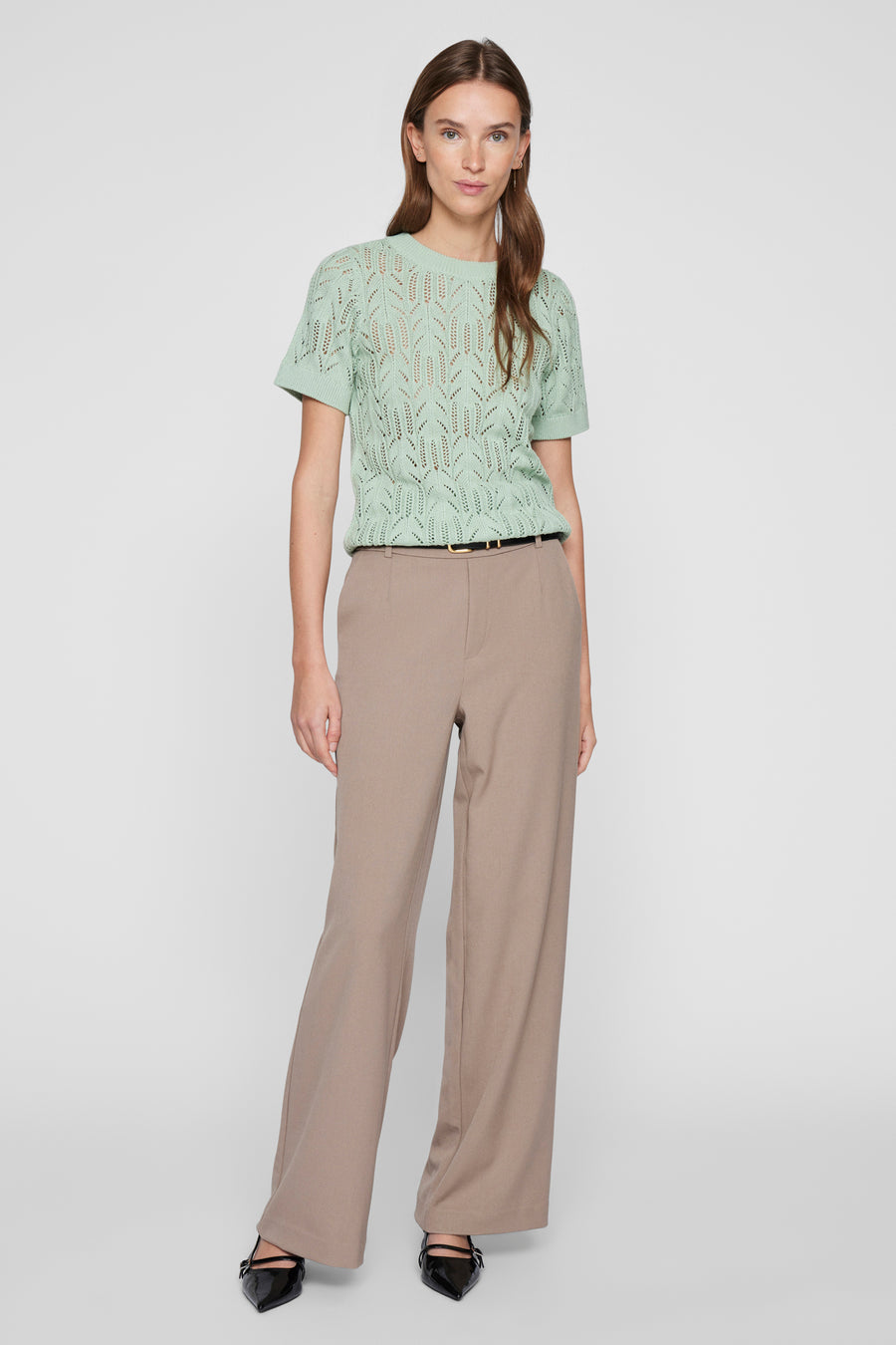 Pull à col rond vert en maille ajourée de VILA, porté avec un pantalon taille haute beige.
