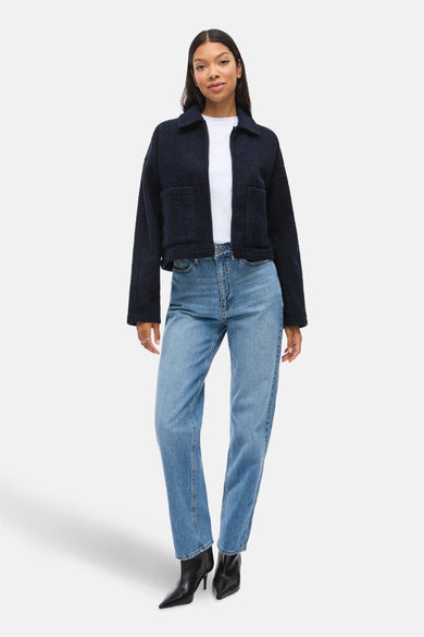 Korte blauwe jas van VILA®, gedragen met een wit T-shirt, een blauwe jeans en zwarte enkellaarsjes.
