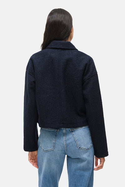 Kort marineblauw textuurjasje van VILA, gedragen met een lichtblauwe high-waist jeans, van achteren gezien.