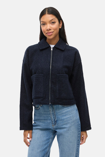 Veste courte bleue de VILA, avec fermeture éclair et poches plaquées, portée avec un jean taille haute.
