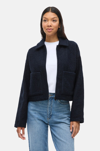 Kort blauw bouclé jasje van VILA, gedragen over een wit T-shirt en een lichtblauwe jeans.