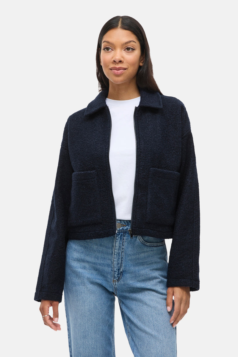 Kort blauw bouclé jasje van VILA, gedragen over een wit T-shirt en een lichtblauwe jeans.