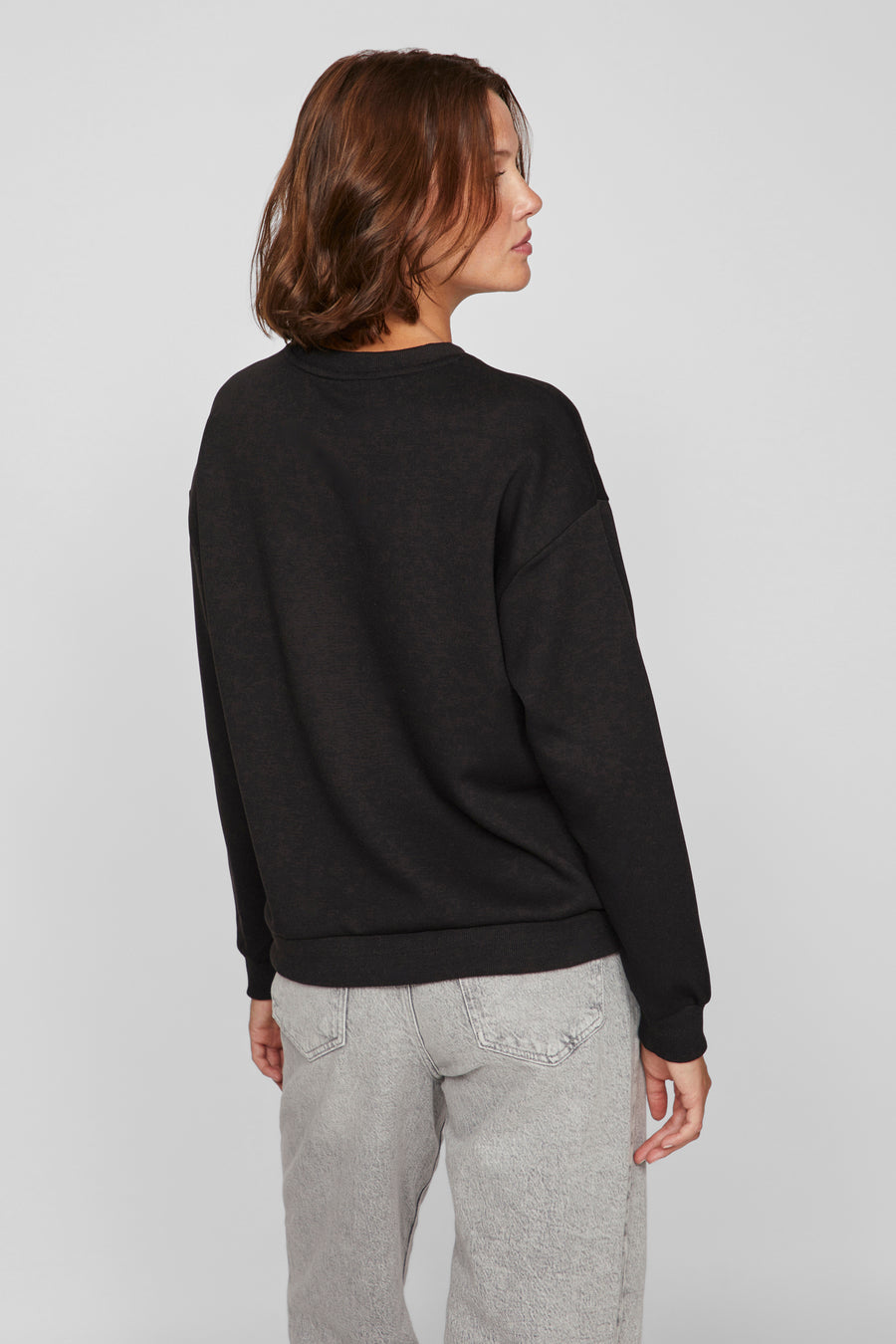 Zwarte trui met ronde hals van VILA, gedragen met een grijze jeans, achterzicht.