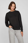 Zwarte rondehals sweatshirt van VILA, gedragen met een lichtgrijze broek, één hand in de zak.