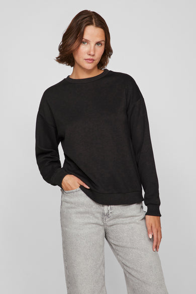 Zwarte rondehals sweatshirt van VILA, gedragen met een lichtgrijze broek, één hand in de zak.