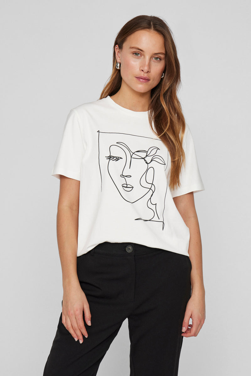 T-shirt blanc à manches courtes de VILA®, orné d'un dessin minimaliste en noir, porté avec un pantalon noir.
