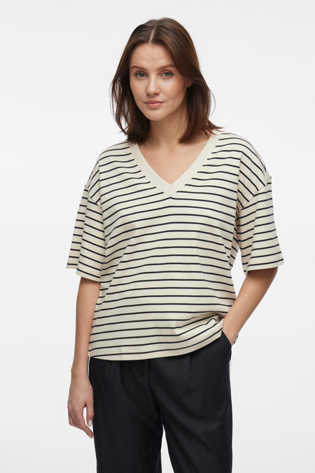 Beige T-shirt met zwarte strepen van VILA, gedragen met een effen zwarte broek, hand in de zak.