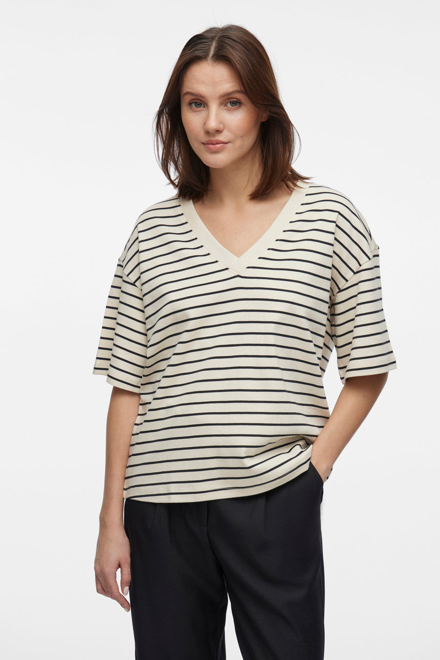 Beige T-shirt met zwarte strepen van VILA, gedragen met een effen zwarte broek, hand in de zak.