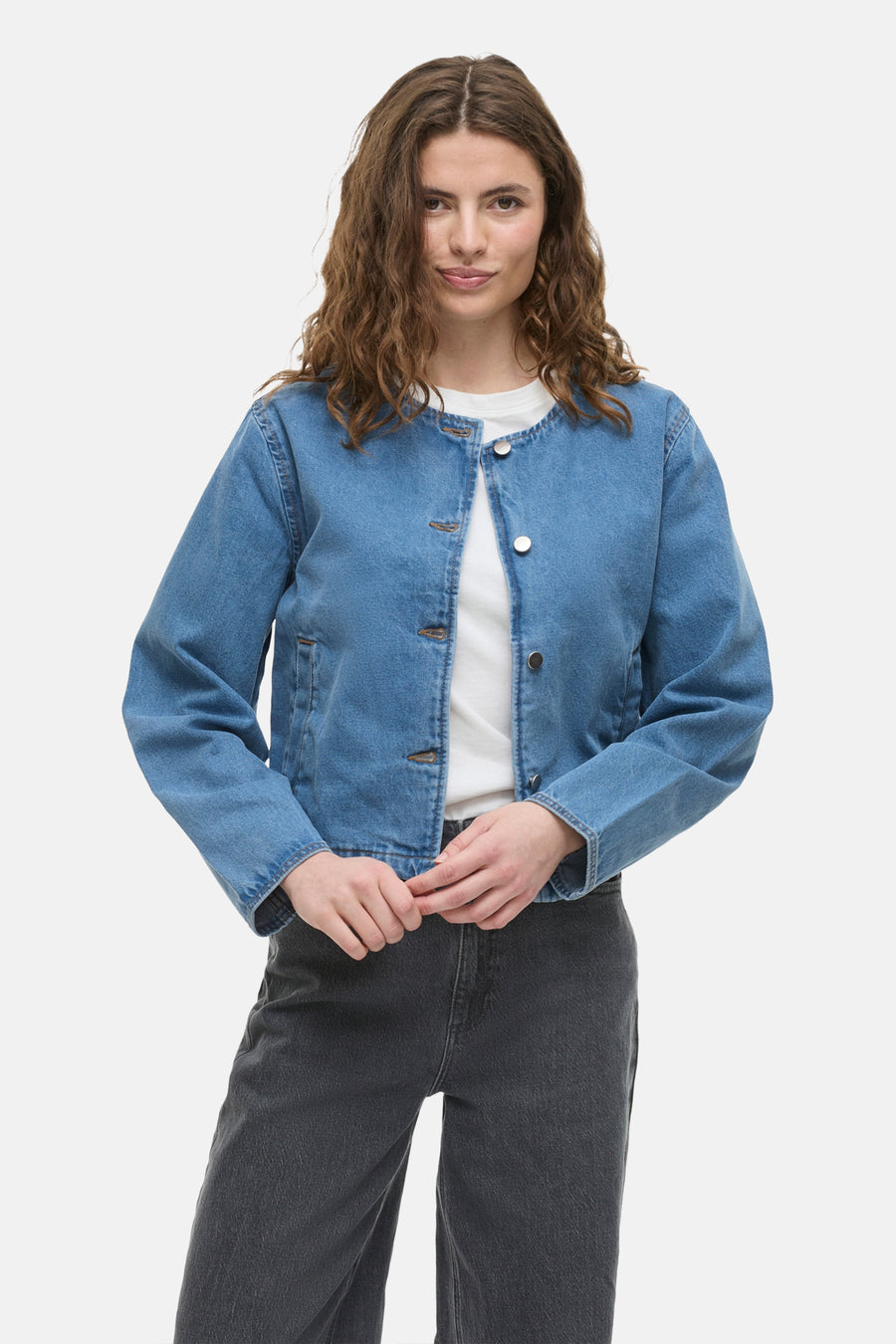 Kort jasje van middieblauw denim van VILA, met zilveren knopen en gedragen over een wit T-shirt.