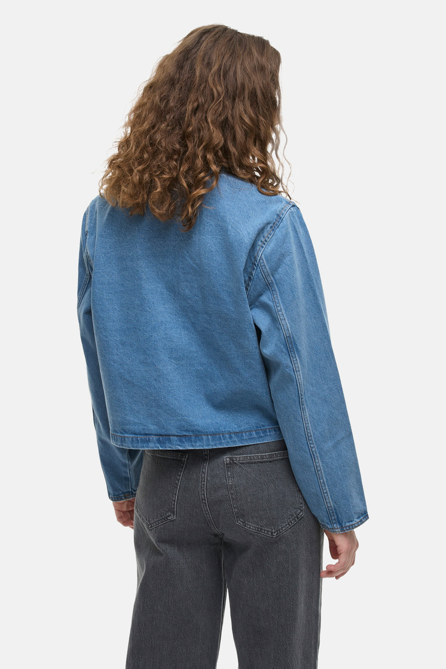 Kort spijkerjack in middieblauw van VILA, van achteren gezien, met een donkergrijze jeans.