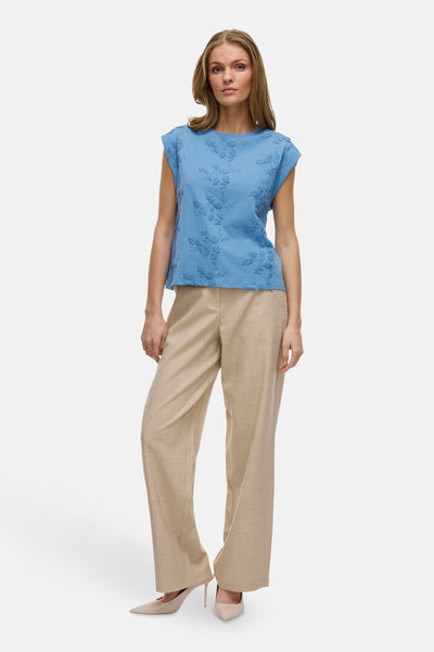 Blauw mouwloos topje van VILA, met bloemenborduursels aan de voorkant, gedragen met een beige broek en pumps.