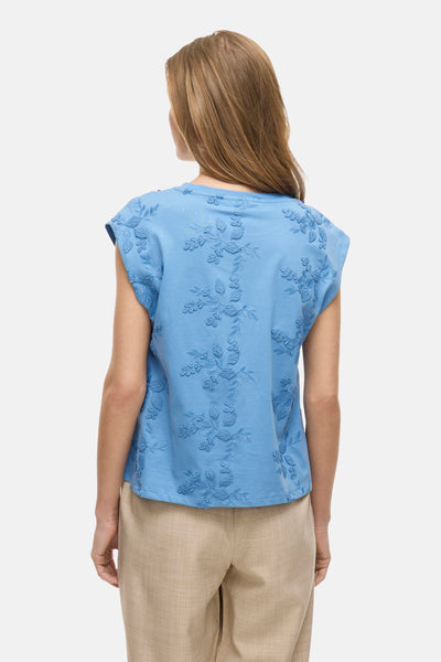 Blauw mouwloos topje van VILA, versierd met een getextureerd bloemenpatroon, gedragen met een beige broek.