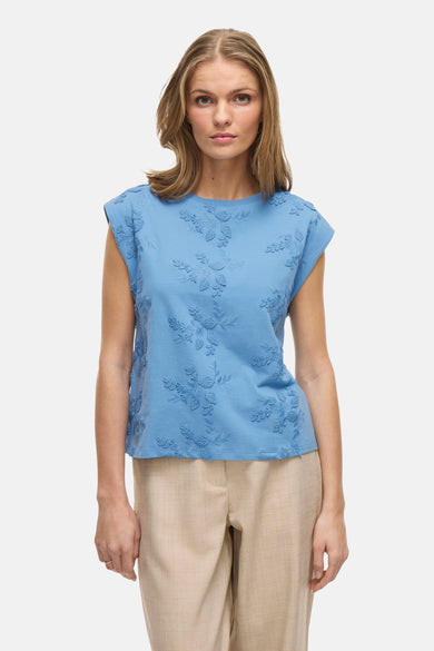 Blauw mouwloos topje VILA® met bloemenborduursels, gedragen met een beige broek.
