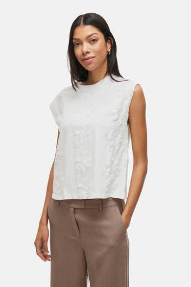 Top sans manches blanc de VILA avec motif floral brodé, porté avec un pantalon taupe.