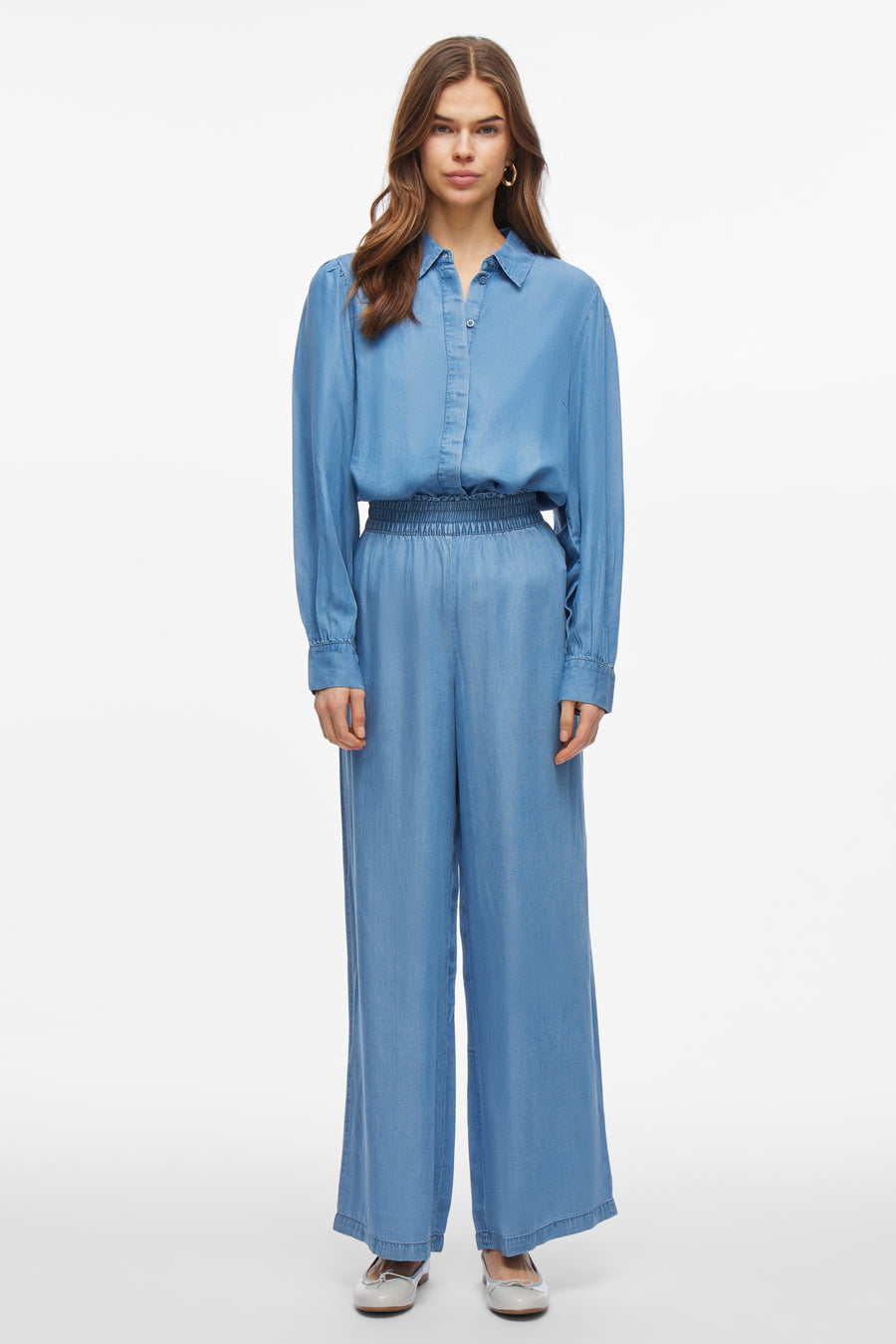 Blouse à manches longues en denim bleu moyen de VILA, portée avec un pantalon ample assorti et des chaussures plates.