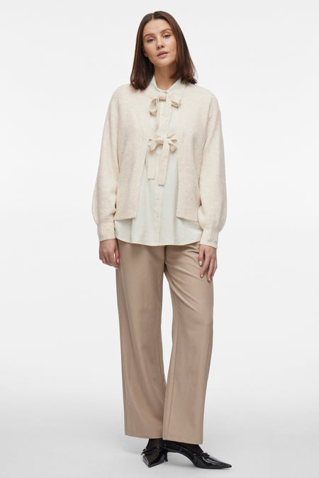 Beige gilet van VILA, gedragen over een lichtgekleurde blouse met strik en een wijde beige broek.