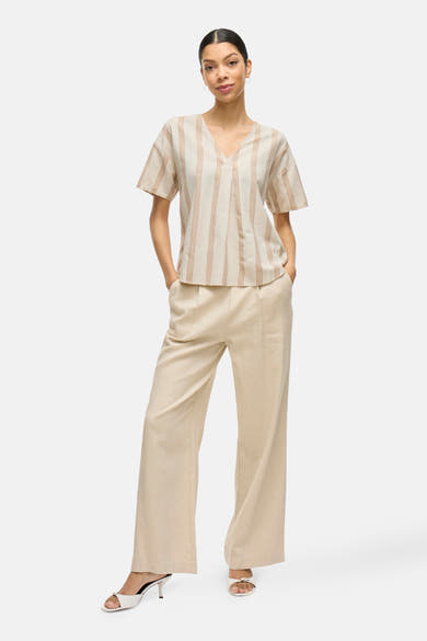 T-shirt beige à rayures verticales de VILA®, porté avec un pantalon ample et des talons ouverts.
