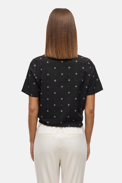 Zwarte blouse met korte mouwen van VILA®, met wit geometrisch patroon en witte broek.